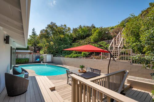 A deck with an umbrella and chairs around the pool